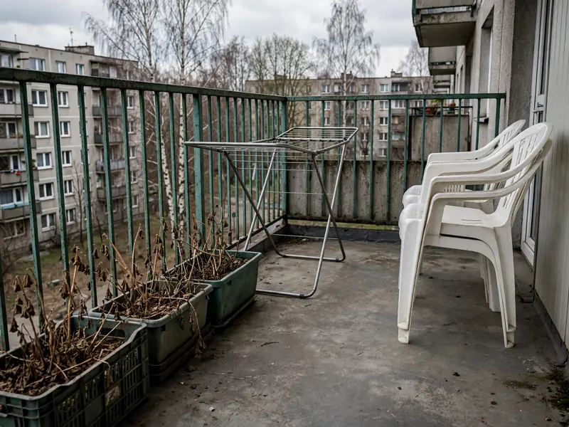 Balkon w bloku ze skrzynkami po kwiatach, suszarką na pranie i plastikowymi krzesłami