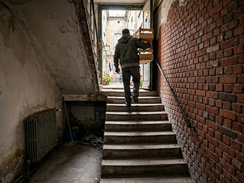 Pracownik wynosi skrzynki z piwnicy kamienicy